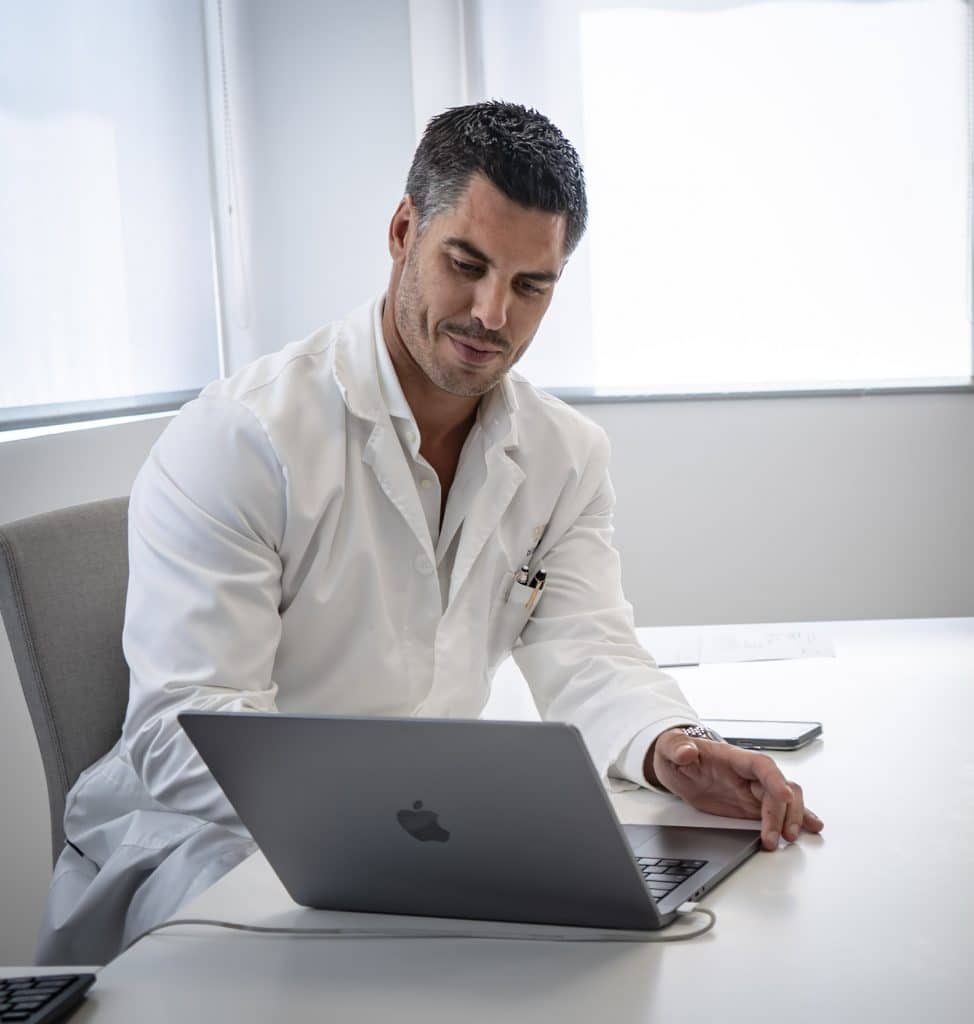 JMF01684 Cirujano plástico del Instituto Rubí revisando información médica en su portátil durante una consulta, en un entorno clínico moderno y luminoso.